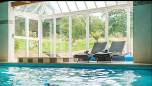 Une piscine avec des chaises longues et un patio fermé par des baies vitrées.