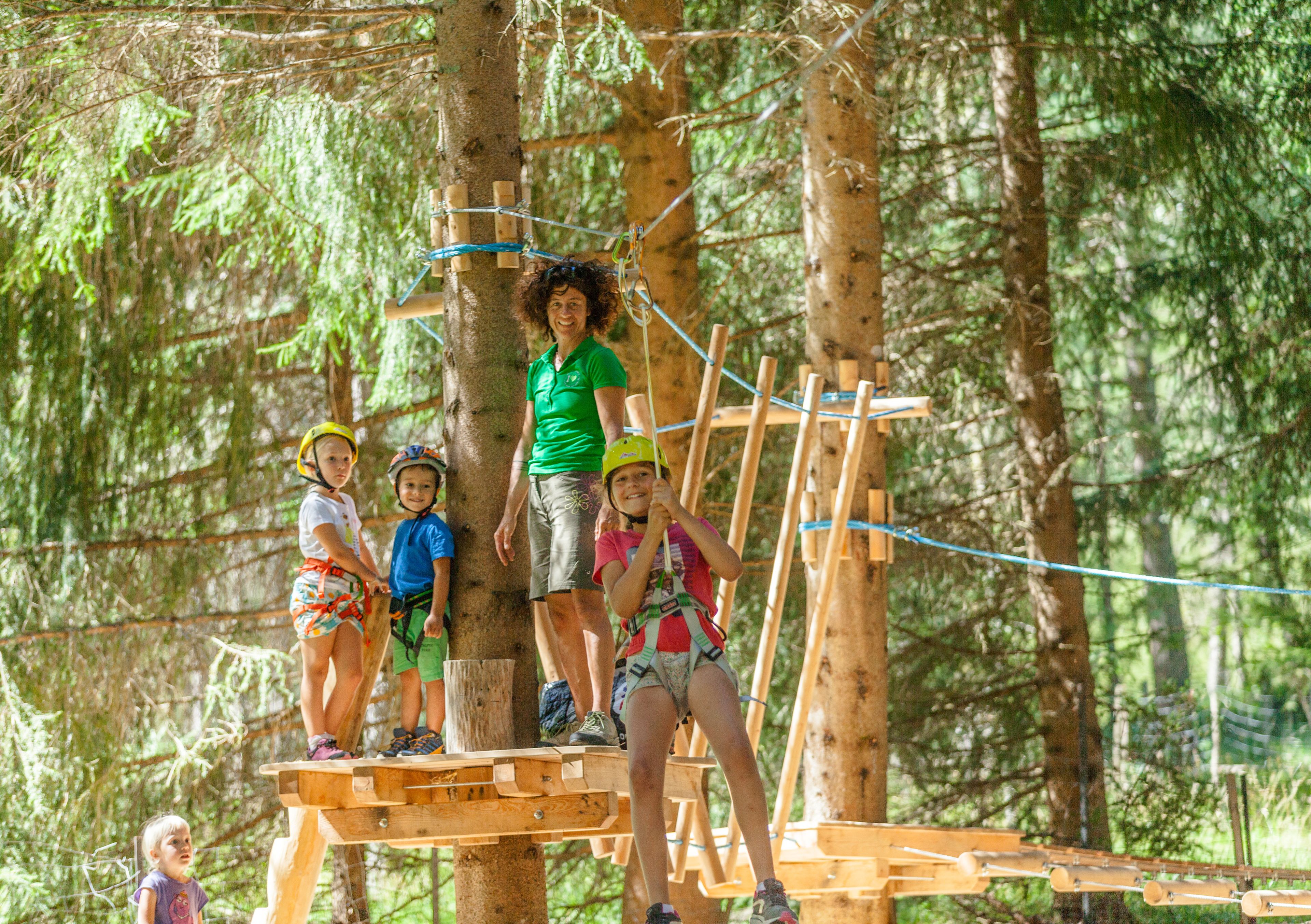 Eine Gruppe von Menschen auf einer Holzplattform in einem bewaldeten Gebiet, mit Seilen und Holzbauten.