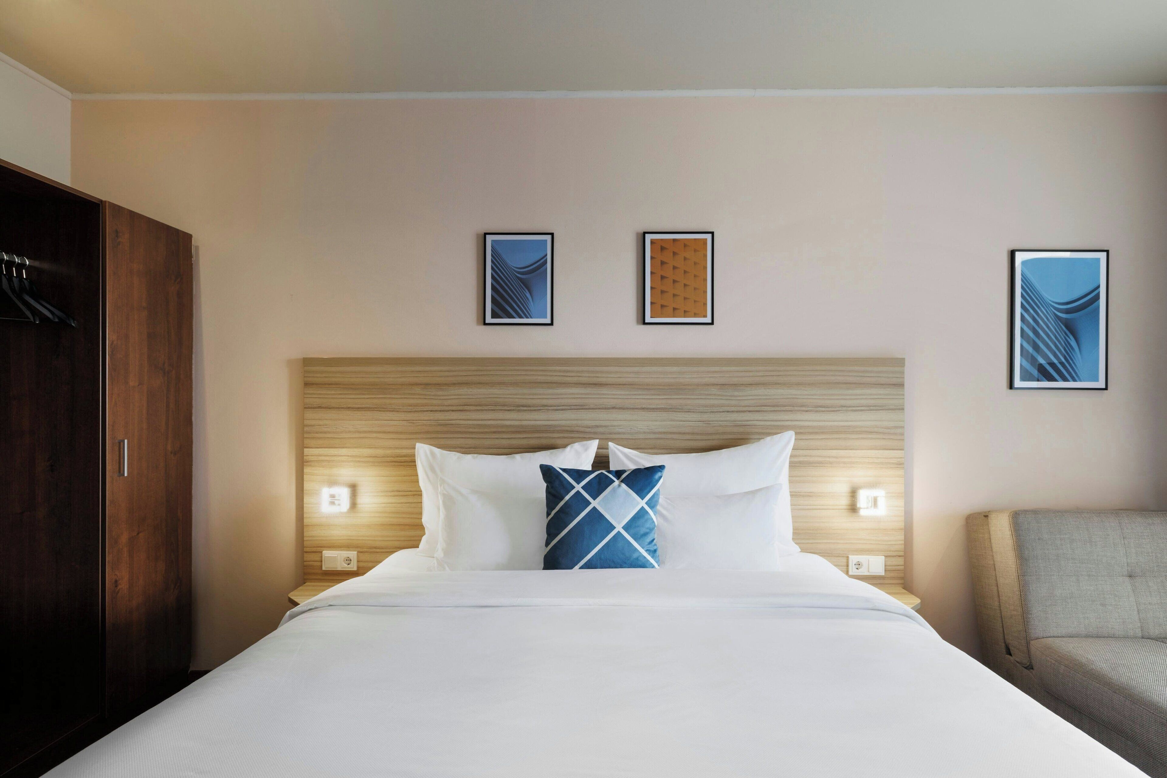 A hotel room with a large bed, a wooden headboard, two wall-mounted lights, and a chair.