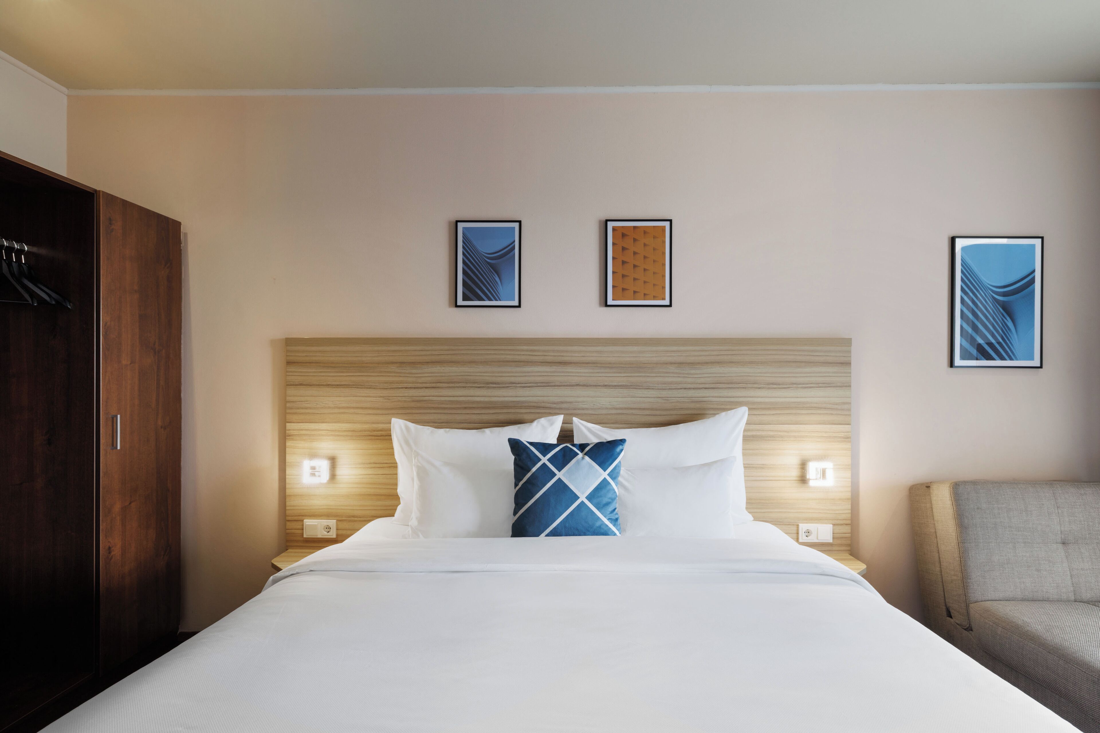 A hotel room with a large bed, a wooden headboard, two wall-mounted lights, and two framed pictures above the bed.