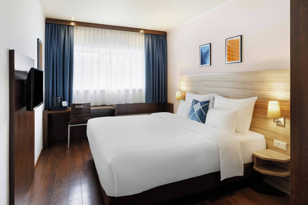 A hotel room with a large bed, a desk, a TV, and a window with curtains.