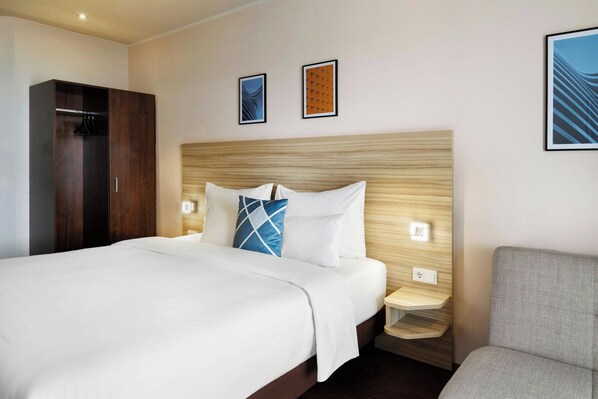 Una habitación de hotel con una cama grande, un armario, una mesita de noche y una silla.