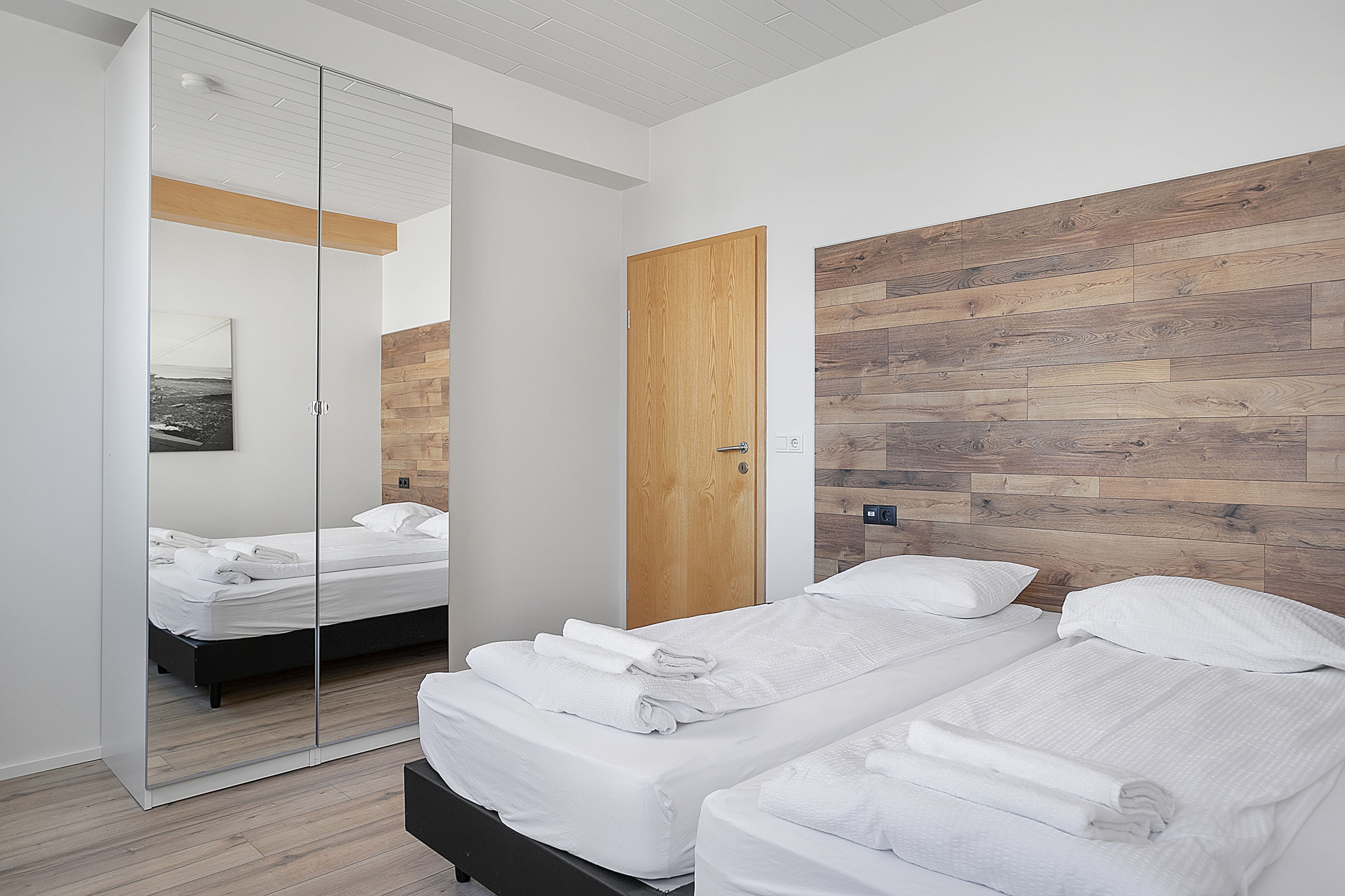 A modern bedroom with two beds, a wooden headboard, a large mirror, and a wooden floor.