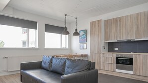 A modern kitchen with wooden cabinets, a built-in oven, and a dining area with a grey sofa and pendant lights. - Stay Apartments Einholt (Reykjavik)