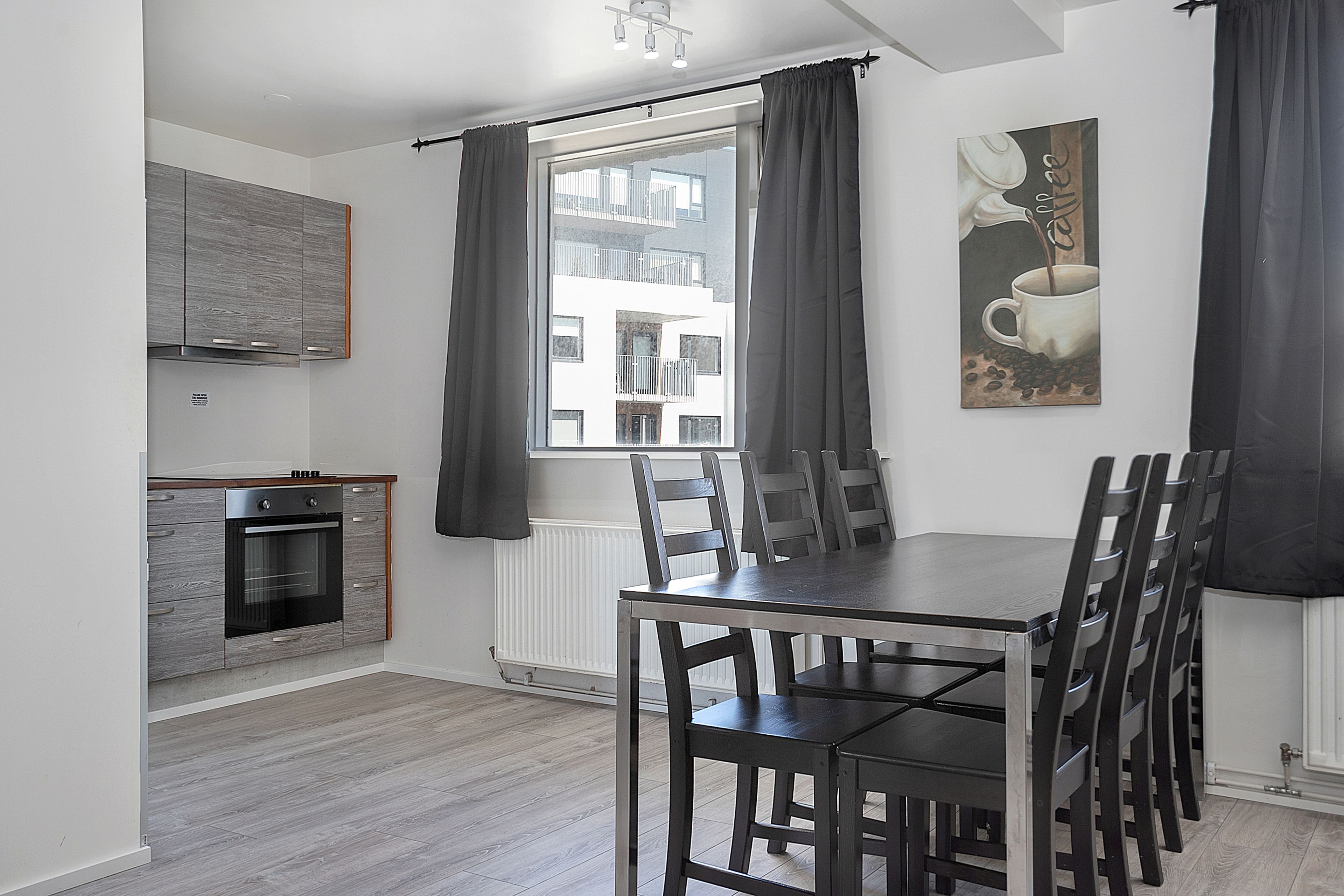 A modern kitchen with grey cabinets, a built-in oven, and a dining area with a dark wooden table and chairs.