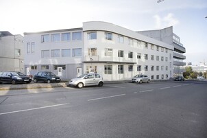 Un edificio moderno con varios pisos y fachada curva. Varios automóviles estacionados en la parte delantera.