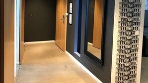A hallway with a modern design, featuring a dark wall with a patterned section, a wooden door, and a framed picture on the wall. - Stay Apartments Einholt (Reykjavik)