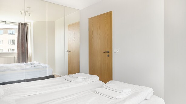 A hotel room with a large mirror, a wooden door, and a bed with neatly folded white towels. - Stay Apartments Einholt (Reykjavik)