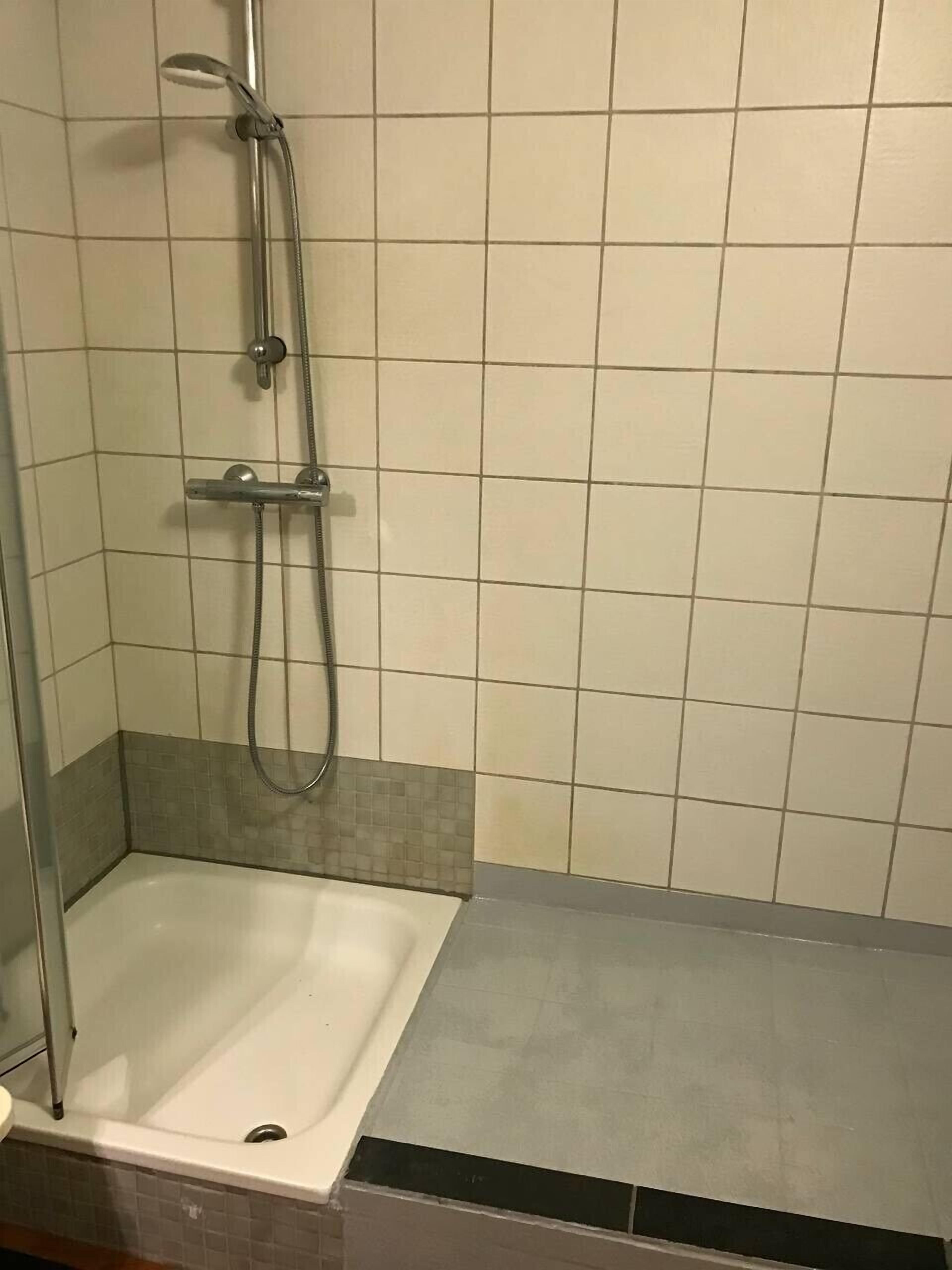 A small, tiled shower area with a handheld showerhead and a handheld shower attachment.