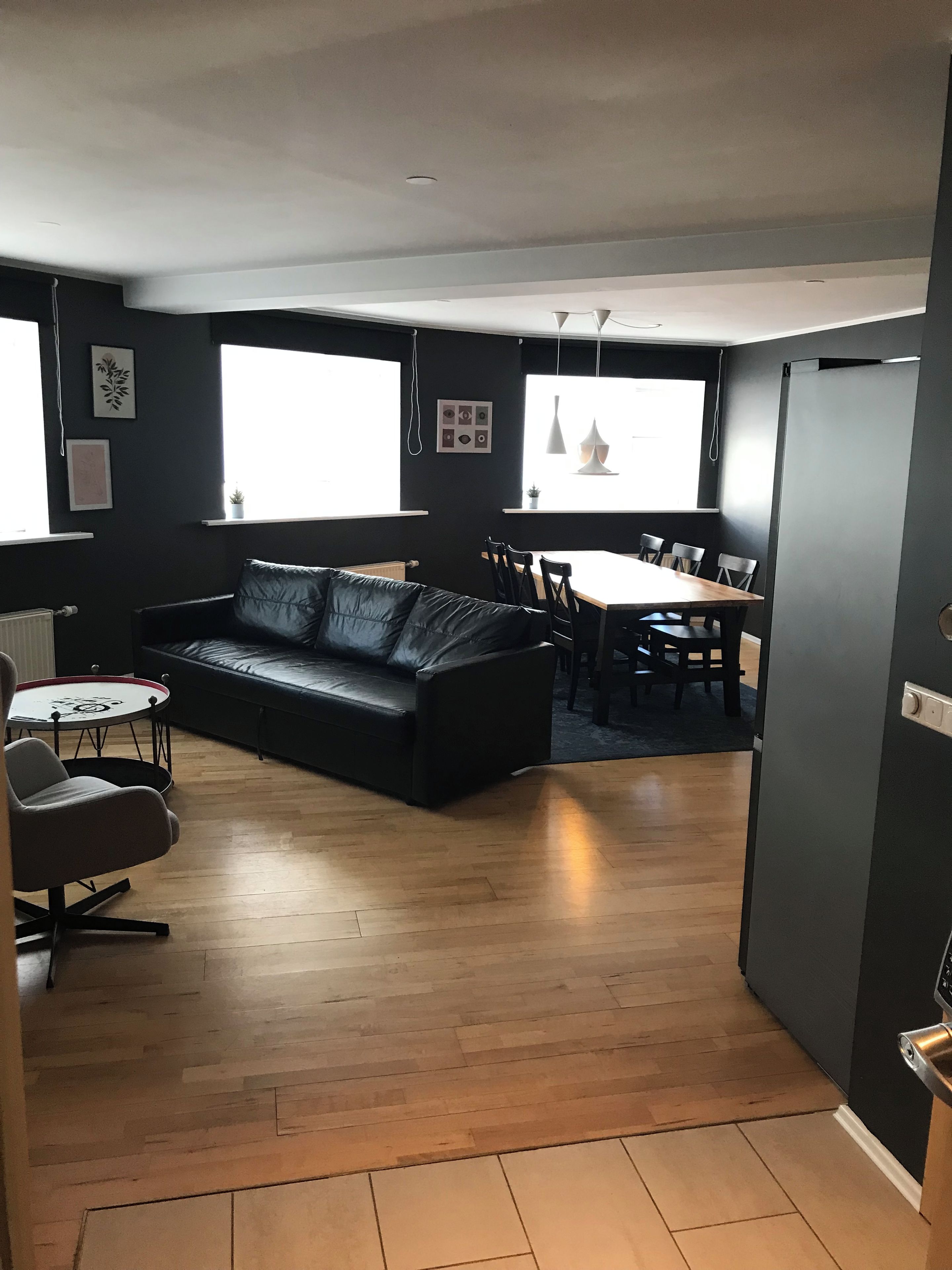 A modern living room with a black leather sofa, a dining table with chairs, and a small round table with a chair.