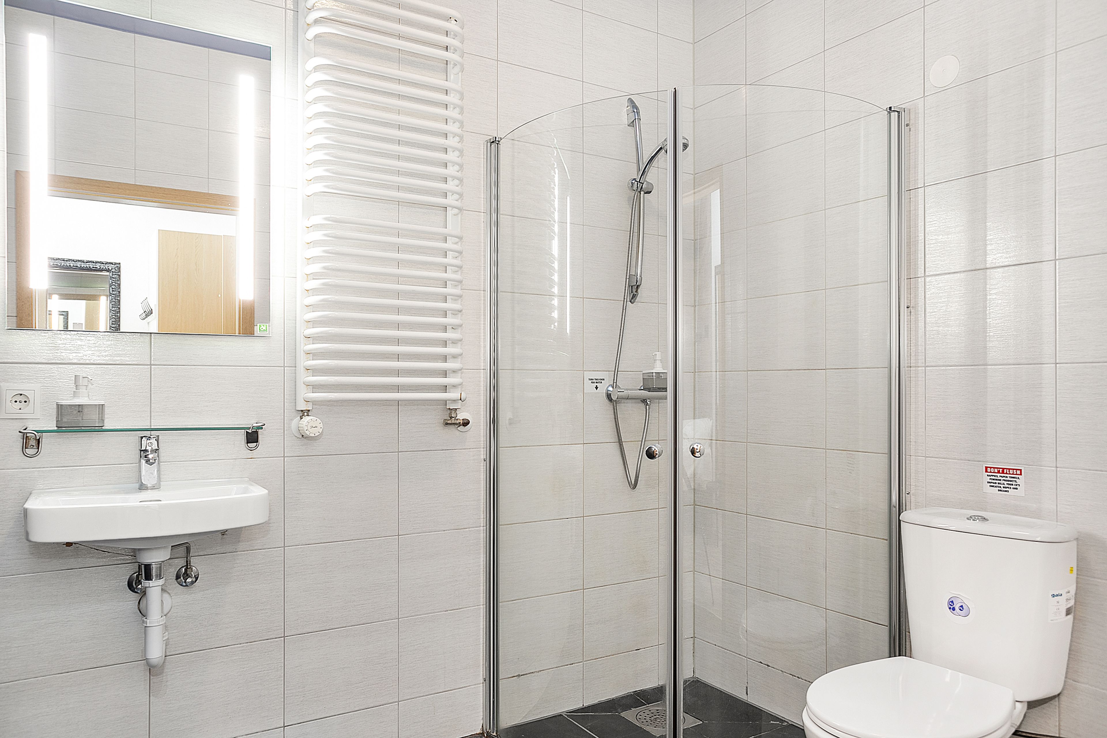 Een moderne badkamer met een douchecabine van glas, een witte wastafel en een toilet.