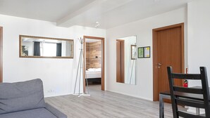 A modern living room with a grey sofa, a wooden dining table with a chair, and a large mirror on the wall. - Stay Apartments Einholt (Reykjavik)