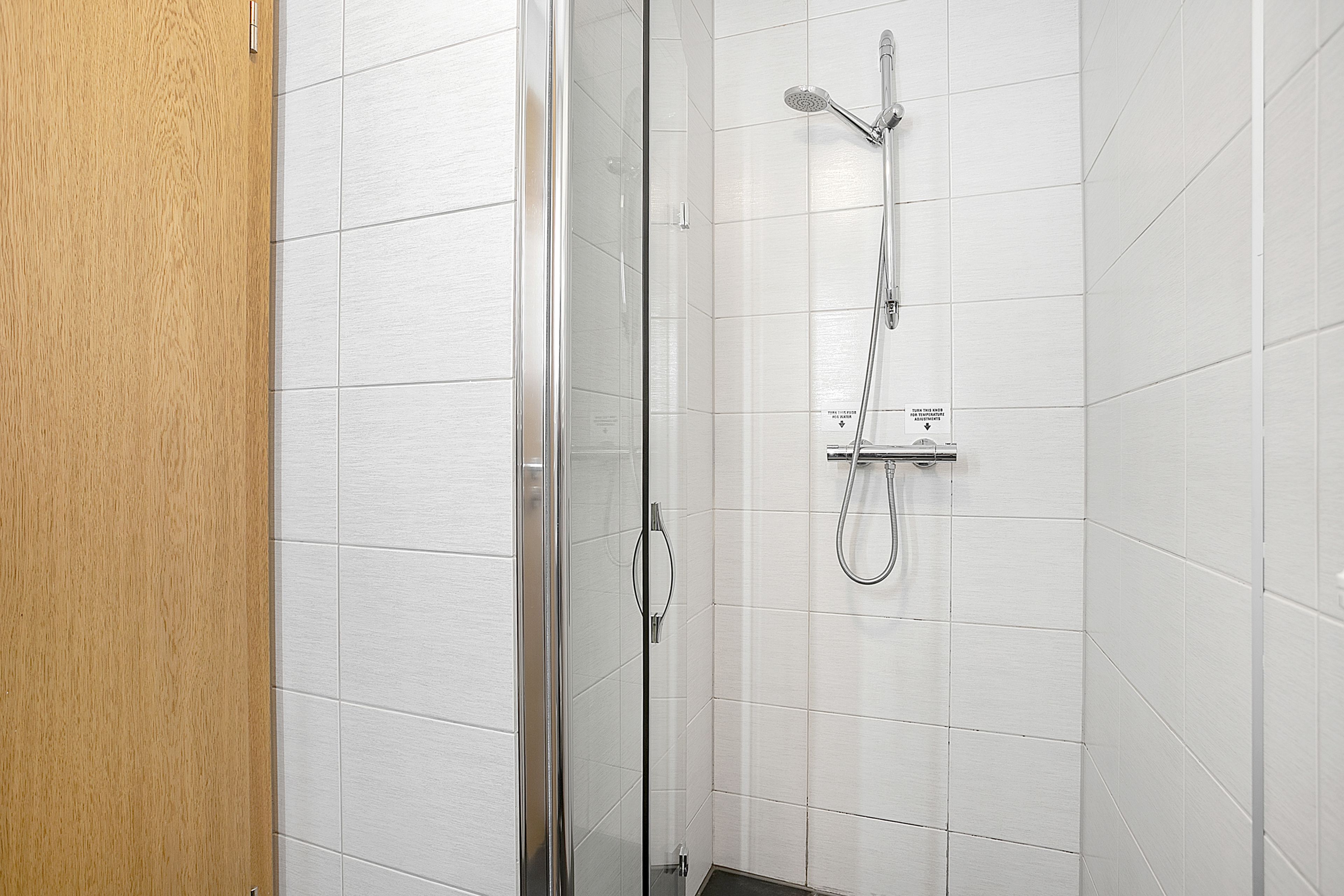 Ducha con mampara de vidrio, cabezal de ducha de mano y grifo empotrado en la pared.