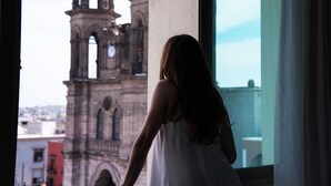 Una persona de pie junto a una ventana con vistas a la torre de una iglesia histórica.