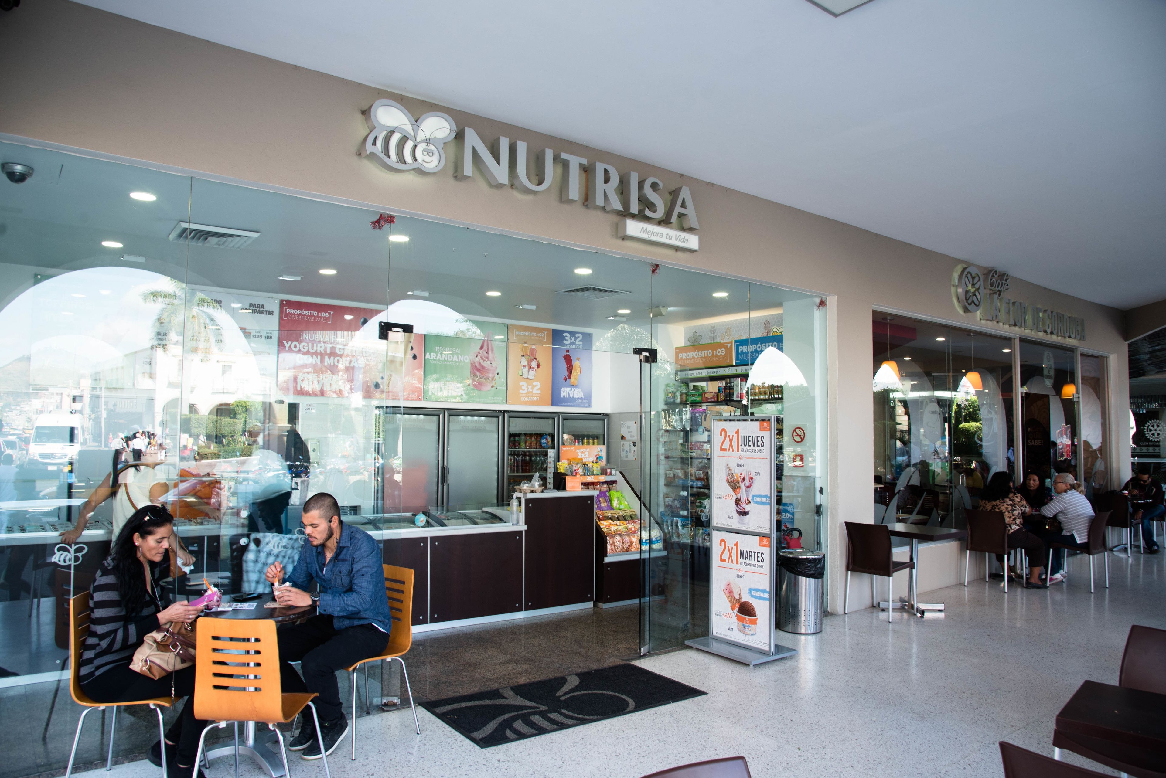 Un café appelé « NUTRISA », doté d’une façade vitrée, d’un espace salon et de panneaux d’affichage où le menu est clairement visible.