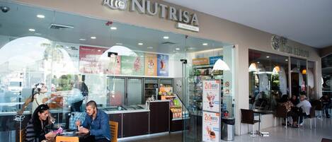 Una cafetería llamada 'NUTRISA' con fachada de vidrio, zona de estar y carteles de menú a la vista.