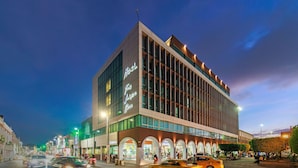 Un hotel moderno con un llamativo letrero que dice 'Hotel', grandes ventanales y un patio central con mesas y sillas.