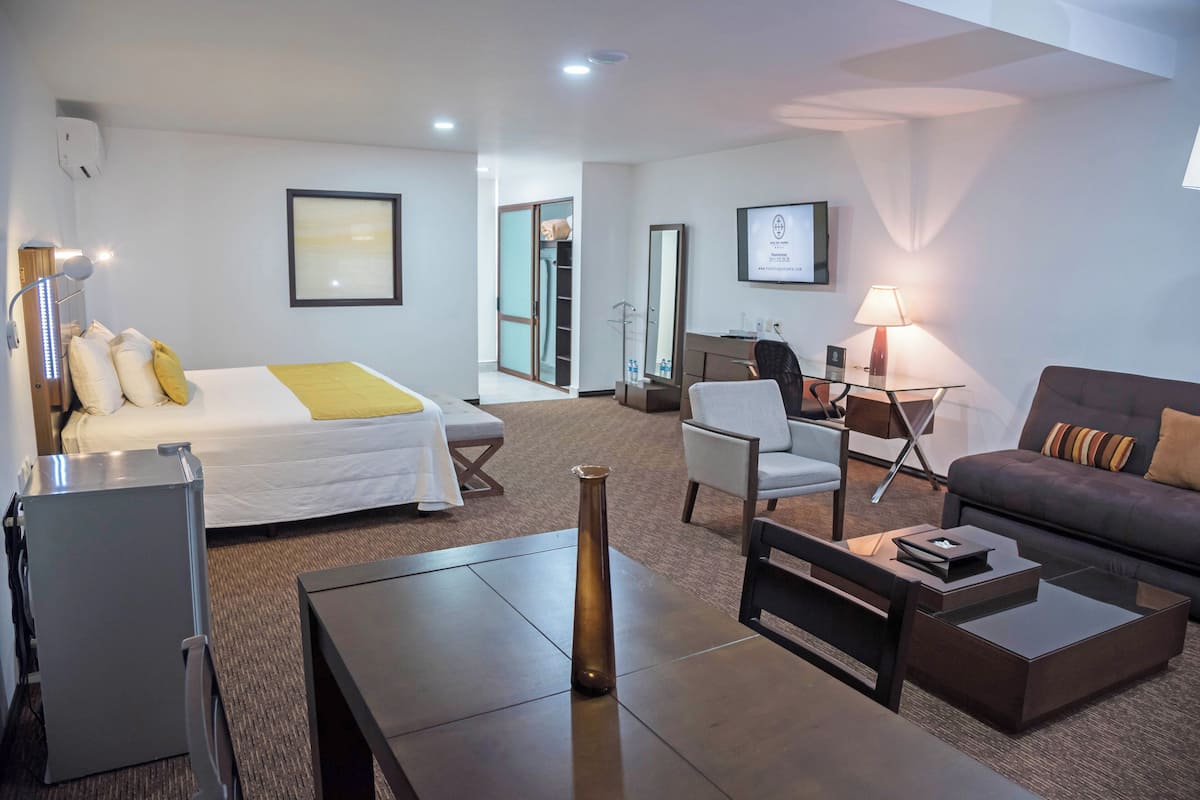 A hotel room with a bed, a desk, a chair, a sofa, a lamp, and a vase.