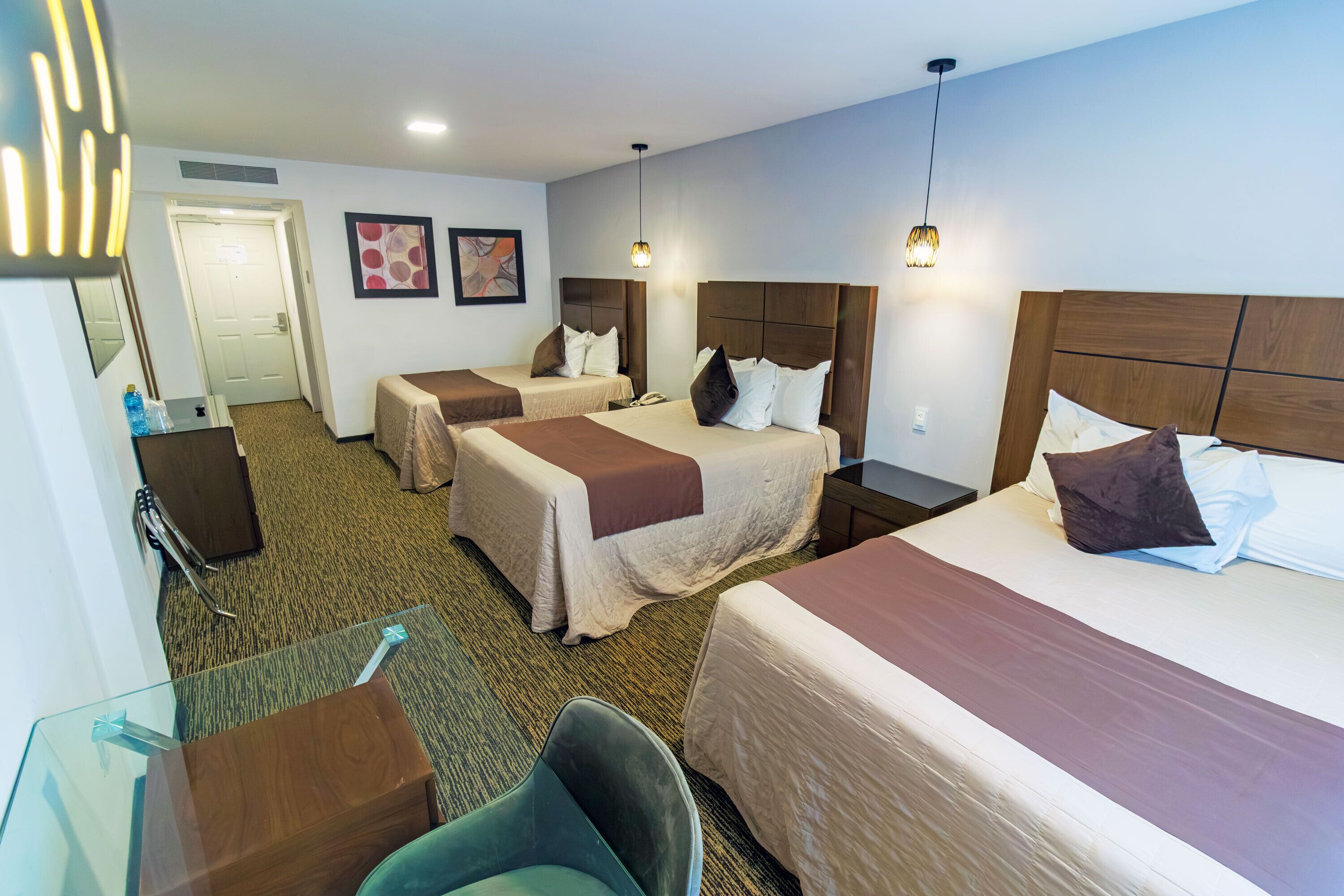 A hotel room with three beds, a desk, a chair, and a door.