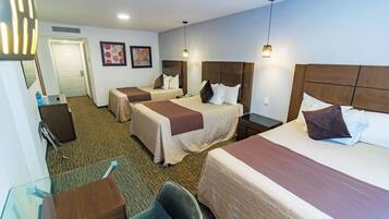 A hotel room with three beds, a desk, a chair, and a door.