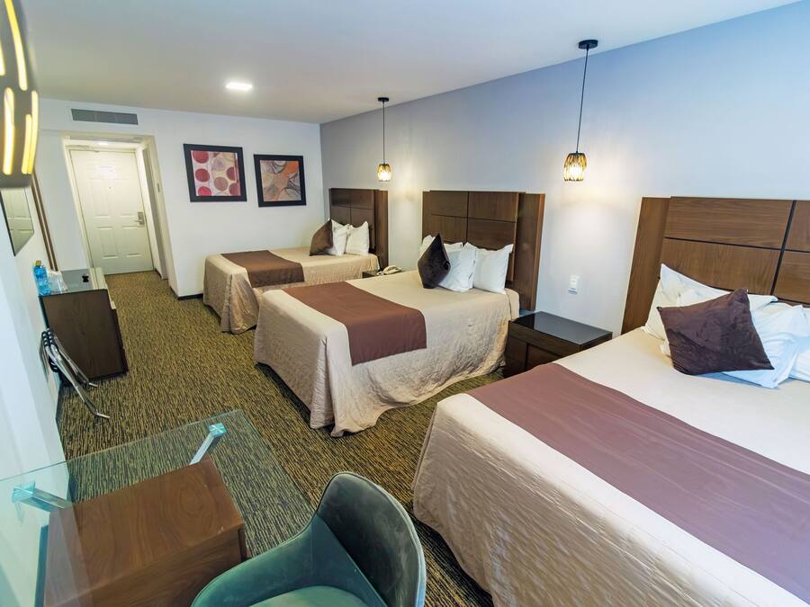 A hotel room with three beds, a desk, a chair, and a door.