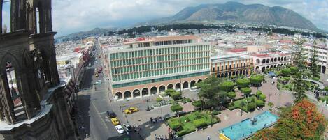 A historic building with a clock tower, a modern building with a courtyard, and a mountainous backdrop.
