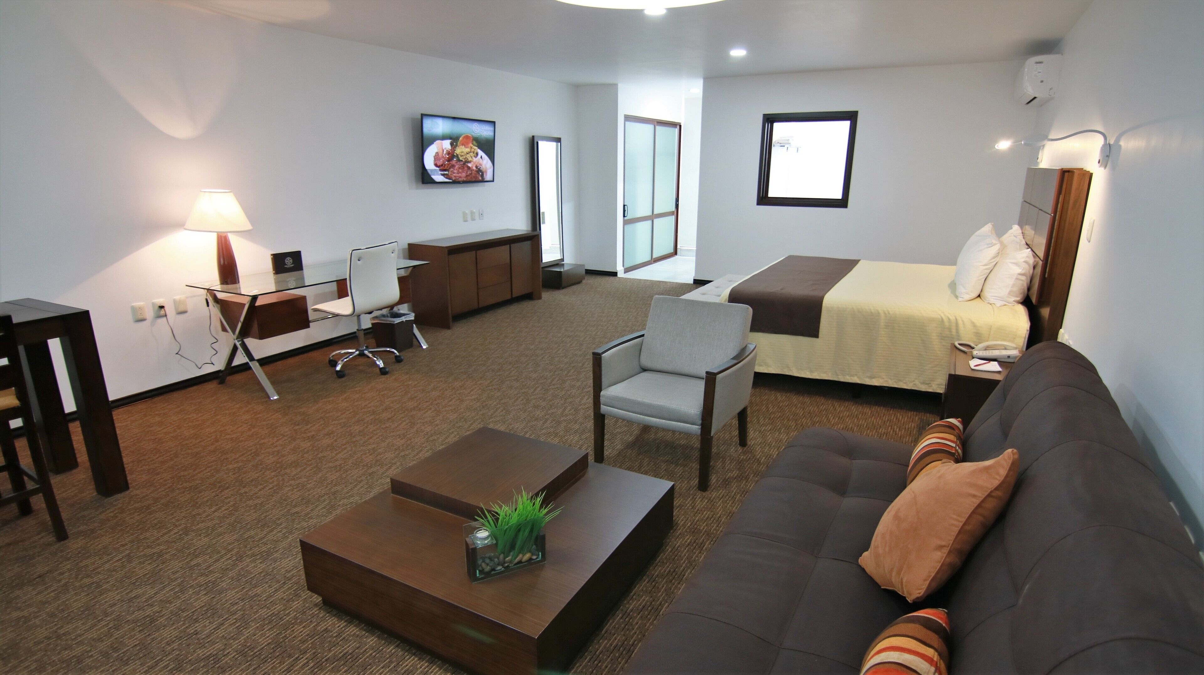 Habitación de hotel moderna con sofá, escritorio, silla, cama y televisor.