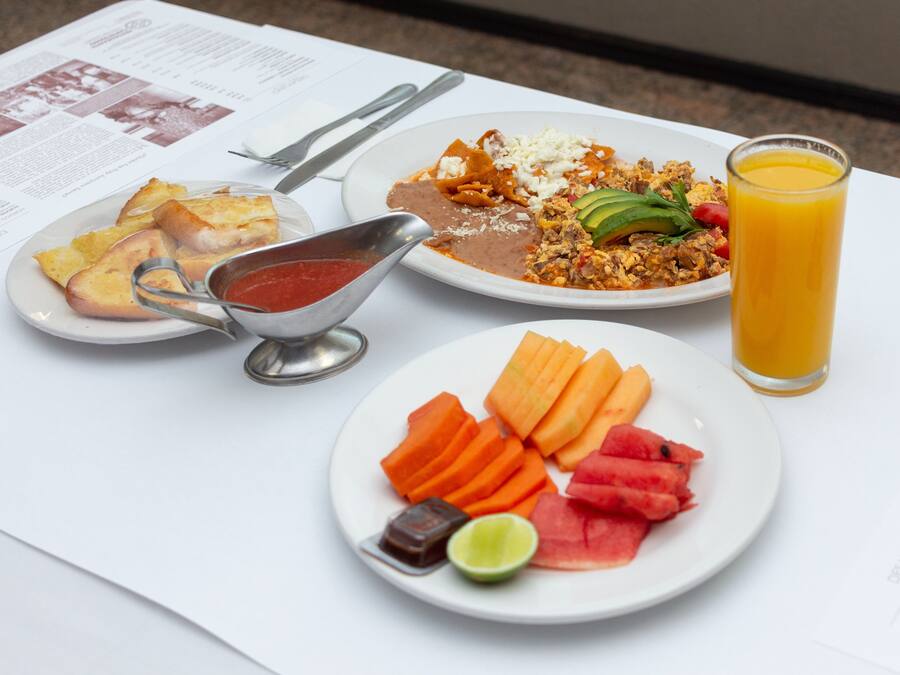 Una mesa con una comida que incluye nachos, un plato de fruta y un vaso de jugo de naranja.