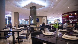 Un restaurante moderno con mesas y sillas ordenadas, una zona de bar y una pantalla de televisión.
