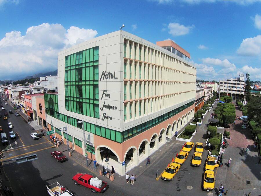 Un gran hotel con un letrero llamativo, varios pisos y un patio central con taxis.