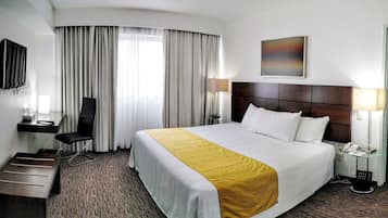 A hotel room with a large bed, a desk with a chair, a TV, and a painting on the wall.