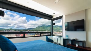 Habitación de hotel con una cama grande, televisión, escritorio y vistas a montañas y una ciudad.