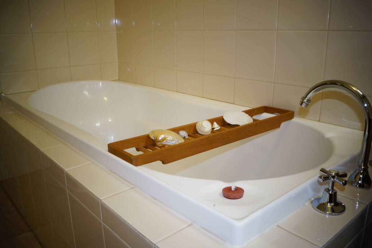 Eine weiße Badewanne mit einem hölzernen Tablett, auf dem eine Kerze, eine Seife und eine kleine Flasche liegen.
