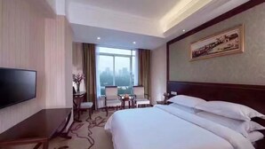 Una habitación de hotel con una cama grande, televisión de pantalla plana, escritorio y vistas a la ciudad desde la ventana.