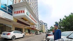 Un hotel llamado "VIENNA" con un letrero, coches estacionados y un guardia de seguridad.