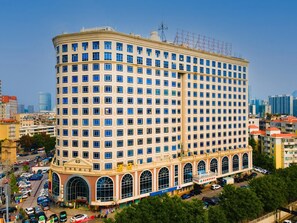Un hôtel à plusieurs étages, doté d’une façade à motifs géométriques, de grandes fenêtres en arc de cercle au rez-de-chaussée et d’un parking situé à l’avant.