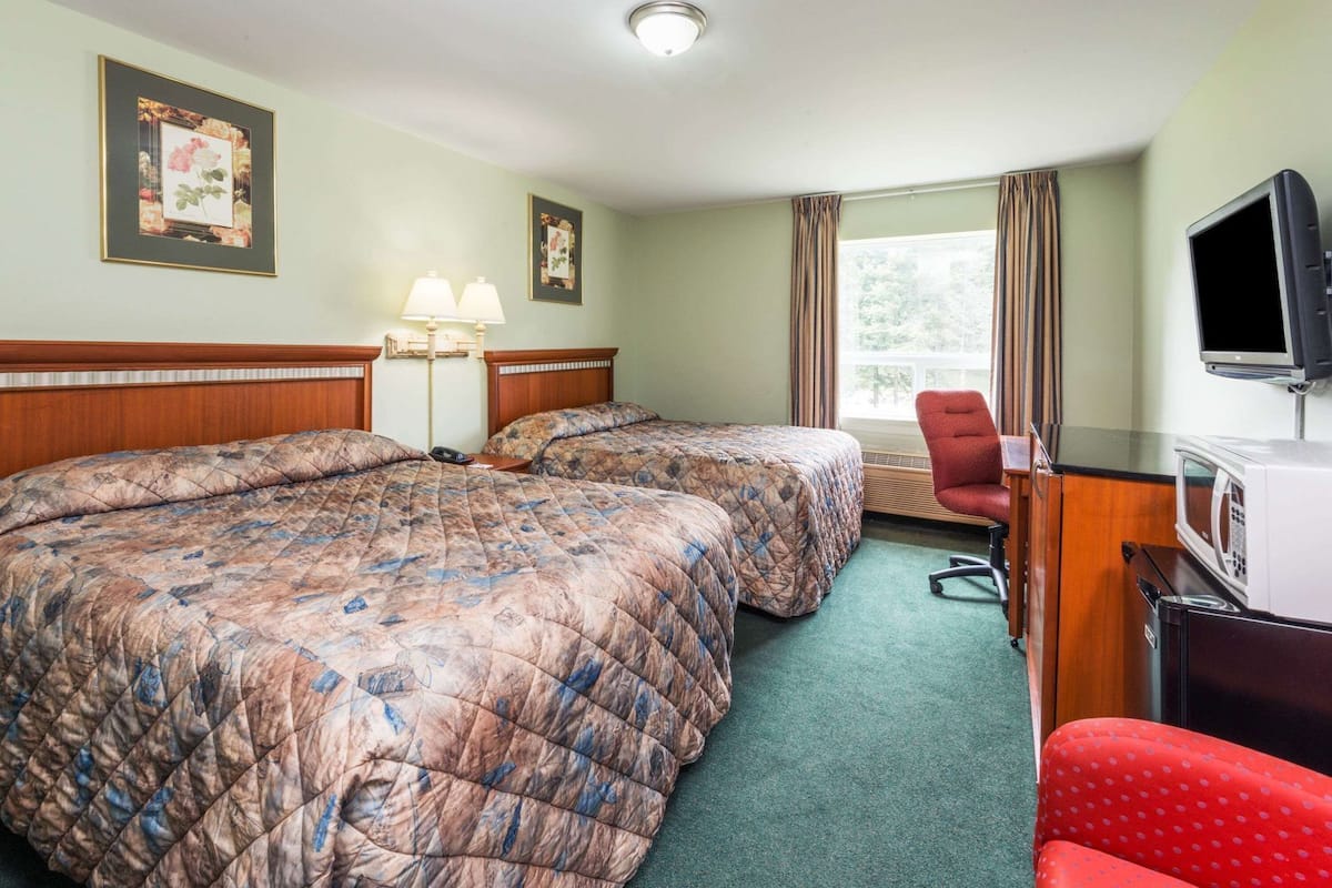 A hotel room with two beds, a desk with a microwave, a TV, and a window with curtains.
