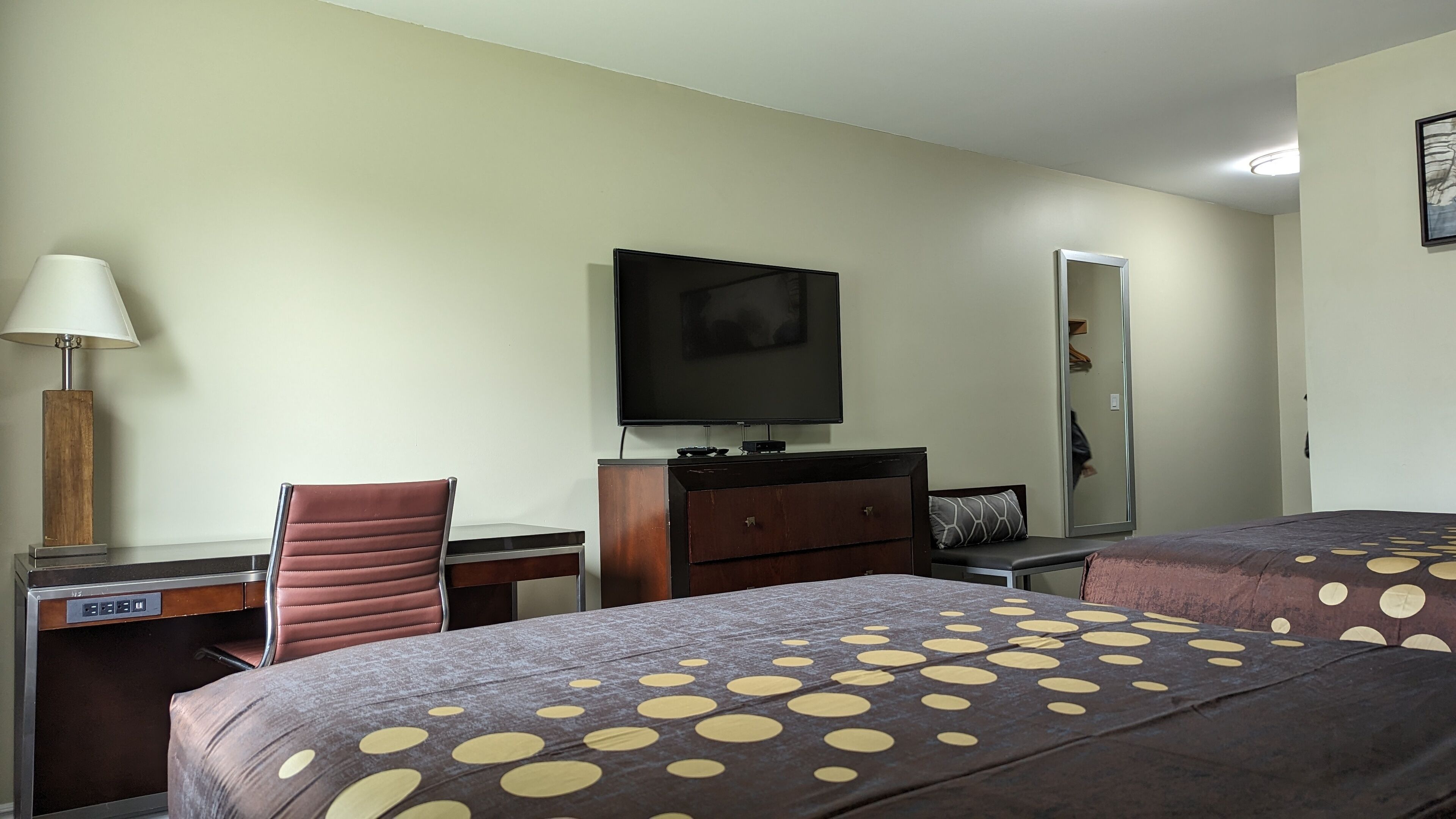 Une chambre d’hôtel équipée d’un bureau, d’une chaise, d’une télévision, d’une commode et de deux lits avec une literie à motifs à pois.