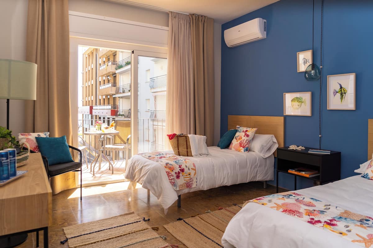 Une chambre d’hôtel avec deux lits, un bureau, une chaise, une petite table et une vue sur le balcon extérieur.