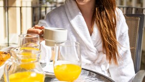 A person in a white robe sitting at a table with a glass of orange juice, a cup, and a plate of food.