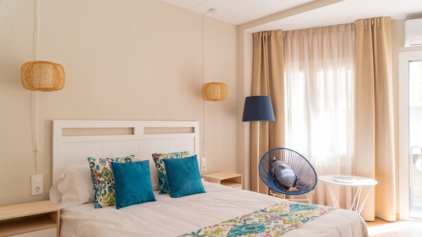 A neatly arranged hotel room with a large bed, two bedside tables, a chair, a small table, and a window with curtains.