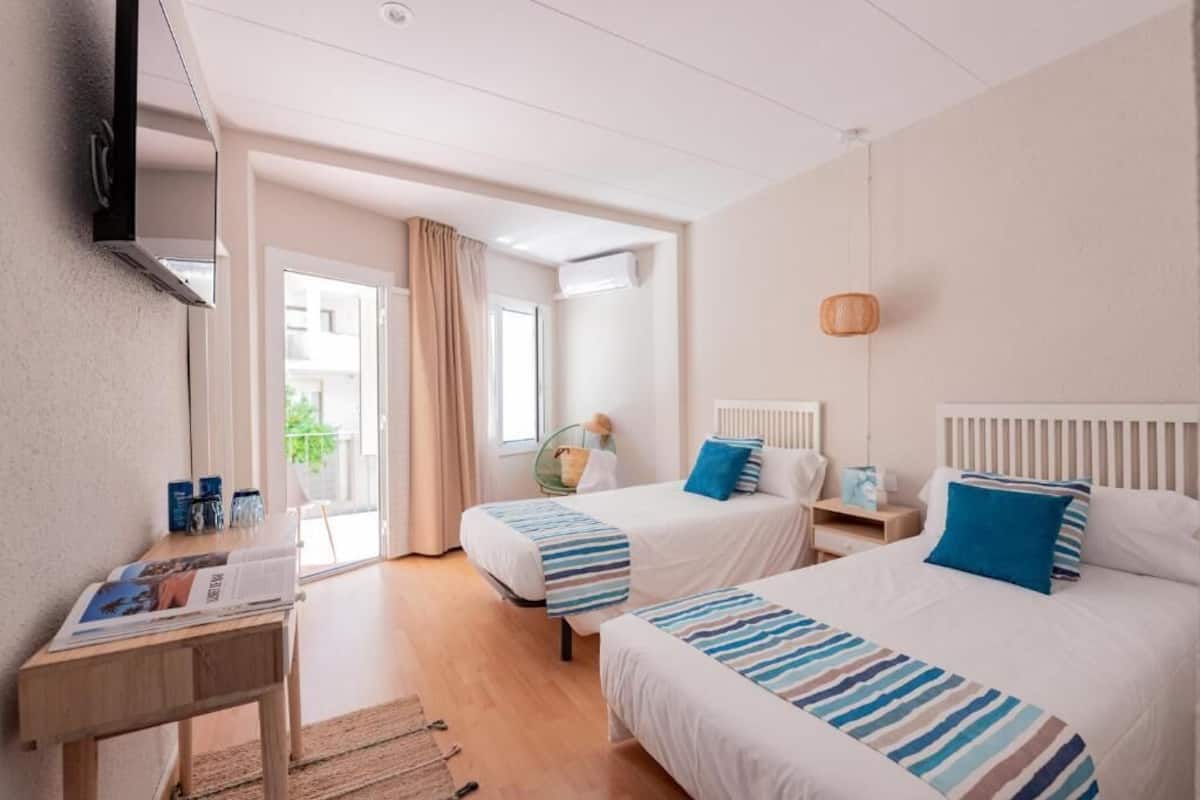 Une chambre d’hôtel avec deux lits, un bureau, une chaise et une fenêtre avec des rideaux.