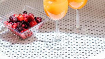 Une table ronde avec deux verres de jus d’orange et un bol de fruits rouges variés.