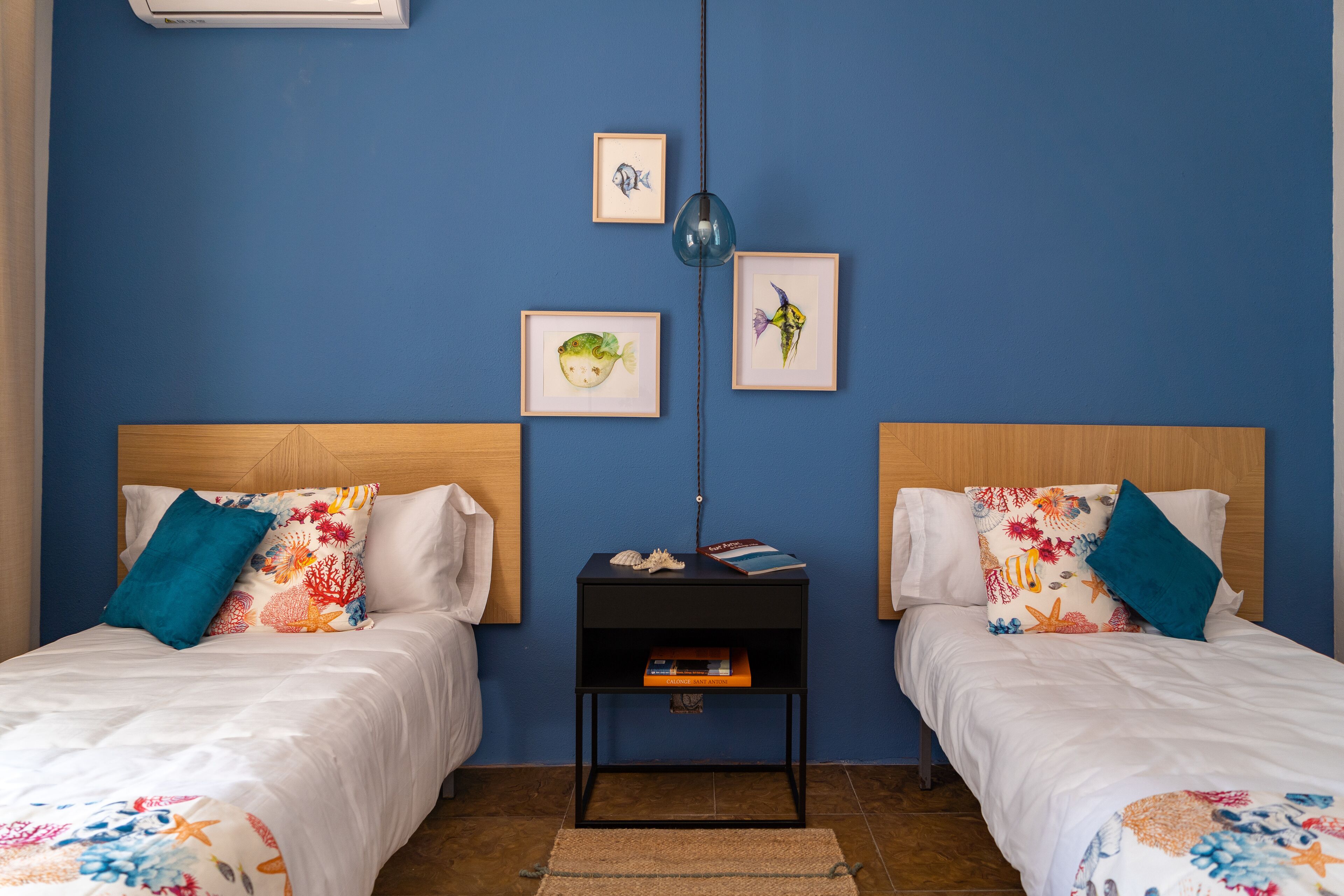 Una habitación con dos camas, una mesita de noche y decoración en la pared.