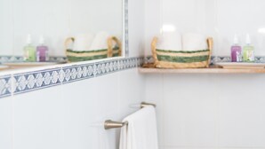 A bathroom with a white sink, a mirror, and a towel rack. There are two shelves above the sink with baskets and toiletries.