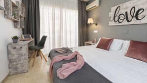 A hotel room with a bed, a desk with a chair, a potted plant, and a wall-mounted air conditioner. - Bulevard Hotel (Castell-Platja d'Aro)