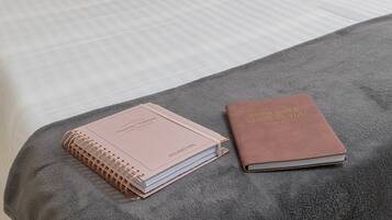 Una cama bien hecha con dos almohadas, una lámpara de noche, una mesita con una vela y un cuaderno sobre la cama.