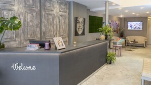 A reception area with a 'Welcome' sign, a reception desk, a television screen, and a seating area with a sofa and chairs. - Bulevard Hotel (Castell-Platja d'Aro)