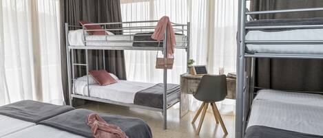 A dormitory room with bunk beds, a desk, and a chair.