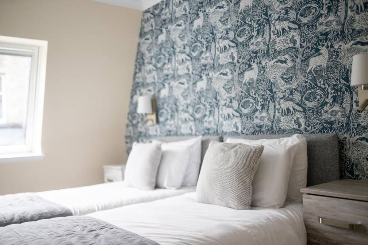 A bedroom with a bed, pillows, a nightstand, and a wall with a patterned wallpaper.